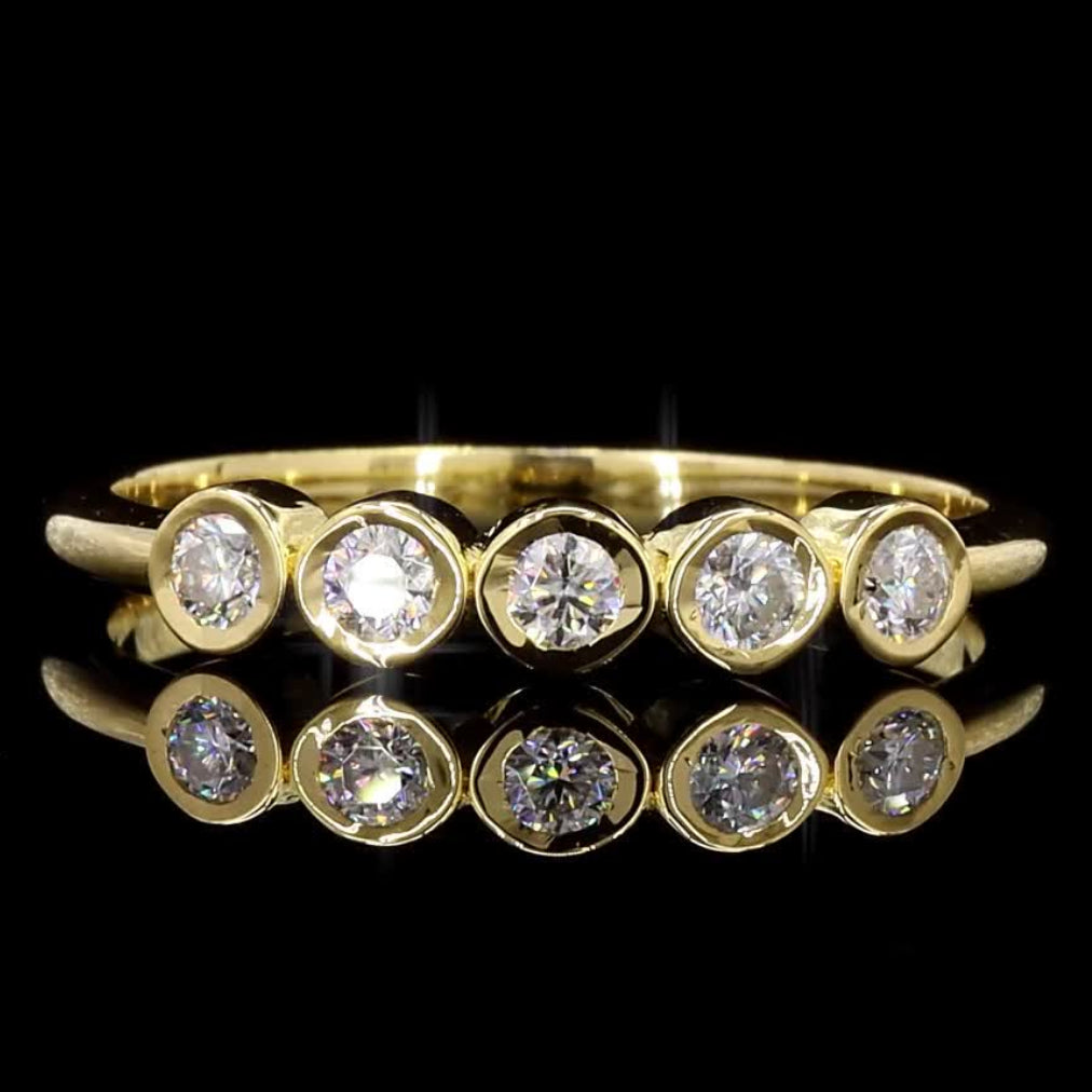 A yellow gold eternity ring featuring five round-cut clear gemstones in a row, displayed against a solid black background with a soft reflection below.