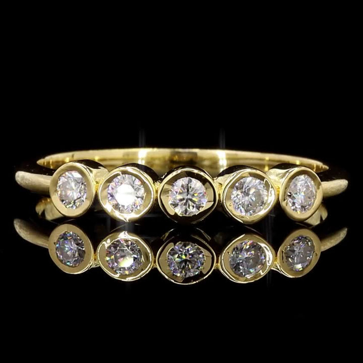 A yellow gold eternity ring featuring five round-cut clear gemstones in a row, displayed against a solid black background with a soft reflection below.