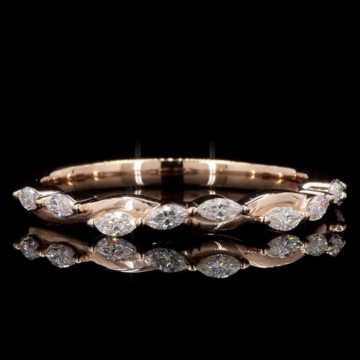 A rose gold eternity band ring set with marquise-cut diamonds, displayed on a reflective black surface against a solid black background.