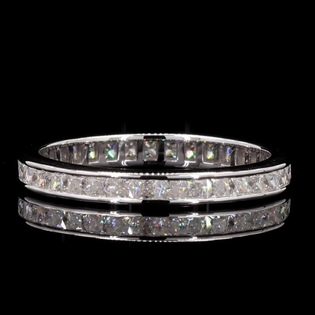 A silver-toned eternity ring set with sparkling clear stones, displayed on a reflective black surface against a solid black background.