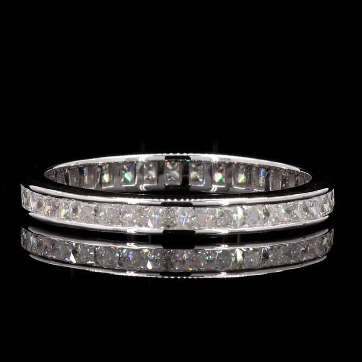A silver-toned eternity ring set with sparkling clear stones, displayed on a reflective black surface against a solid black background.