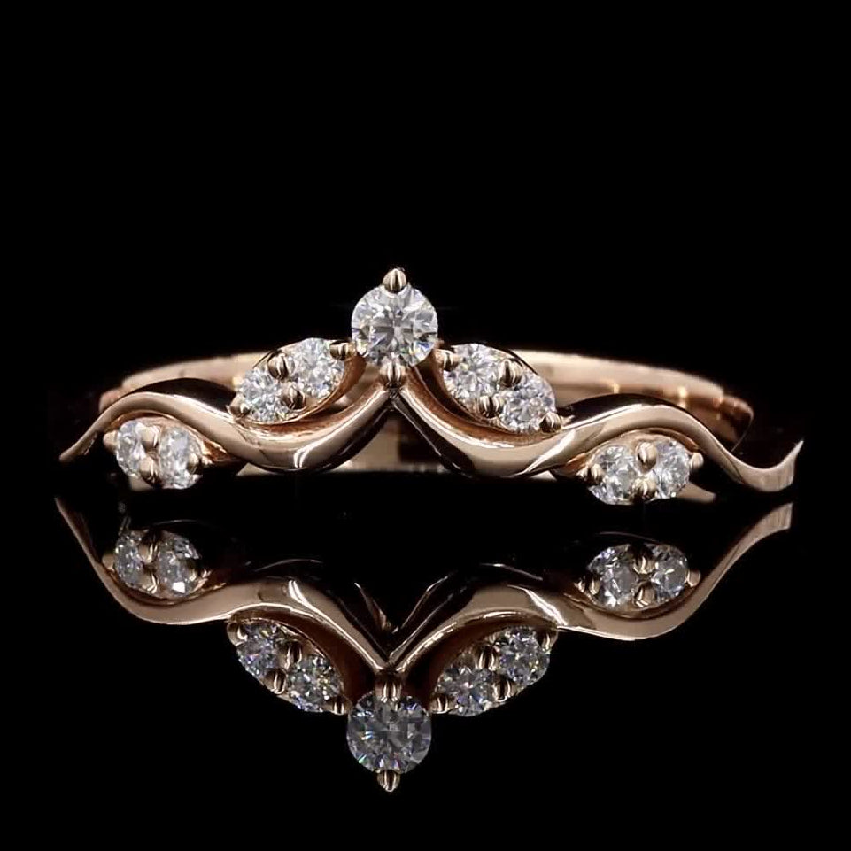 A rose gold ring with a wavy open band design, accented by clear marquise and round-cut gemstones, displayed on a reflective black surface against a black background.