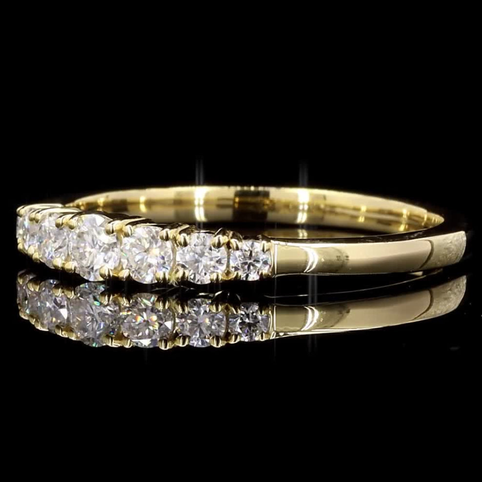 A yellow gold diamond ring with a row of round-cut diamonds, shown on a reflective black background.