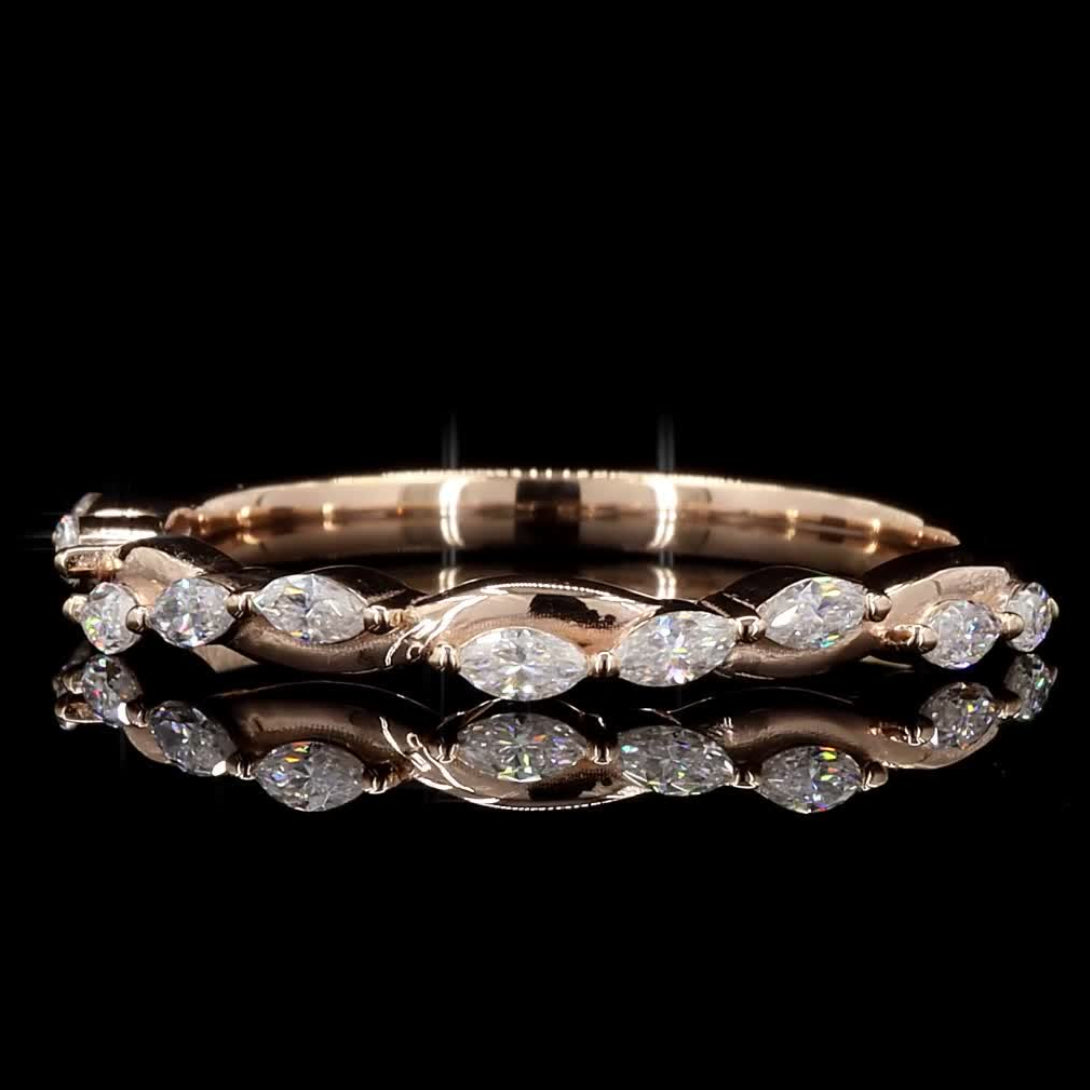 A rose gold eternity band ring featuring marquise-cut clear gemstones, displayed on a reflective black surface against a solid black background.