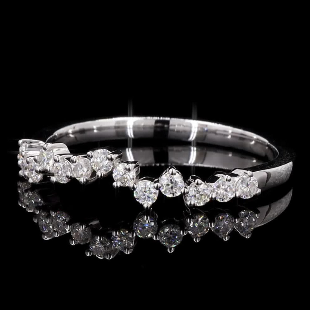A diamond ring with a row of round-cut diamonds set in a polished silver-colored band, displayed on a reflective black surface against a black background.