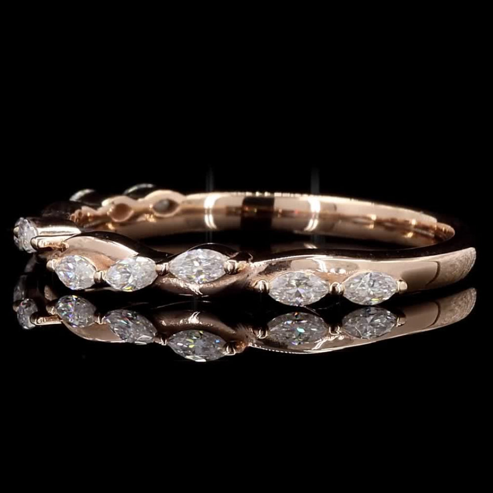 A rose gold eternity-style ring featuring marquise-cut clear gemstones set along the band, shown against a solid black background with a soft reflection below.