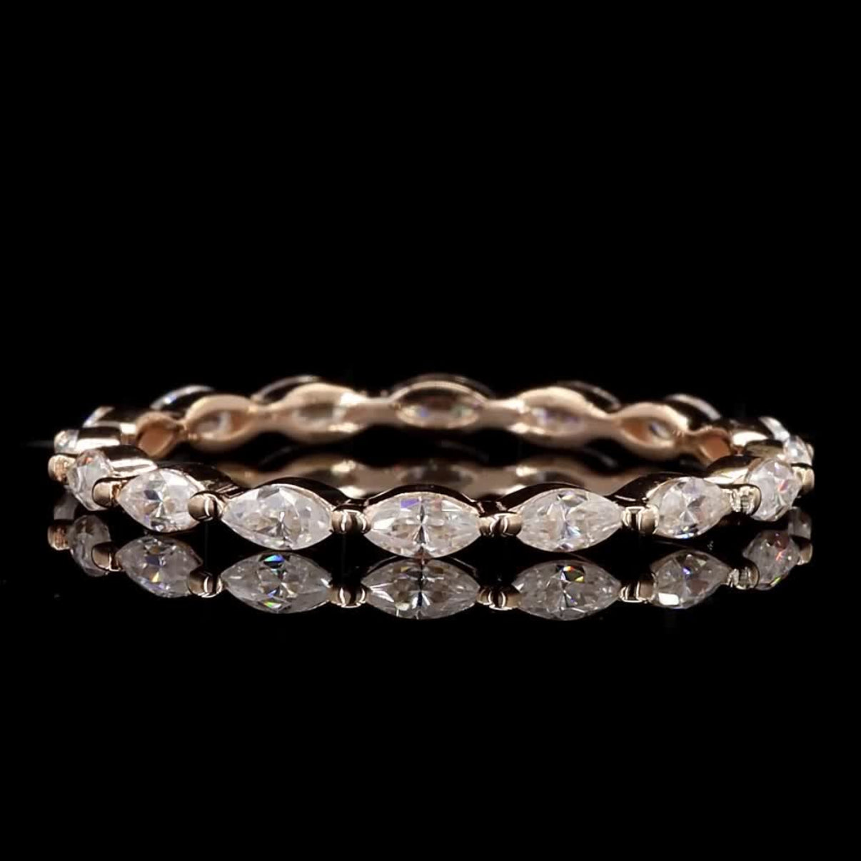 A rose gold eternity ring featuring marquise-cut clear gemstones, displayed on a reflective black surface against a solid black background.