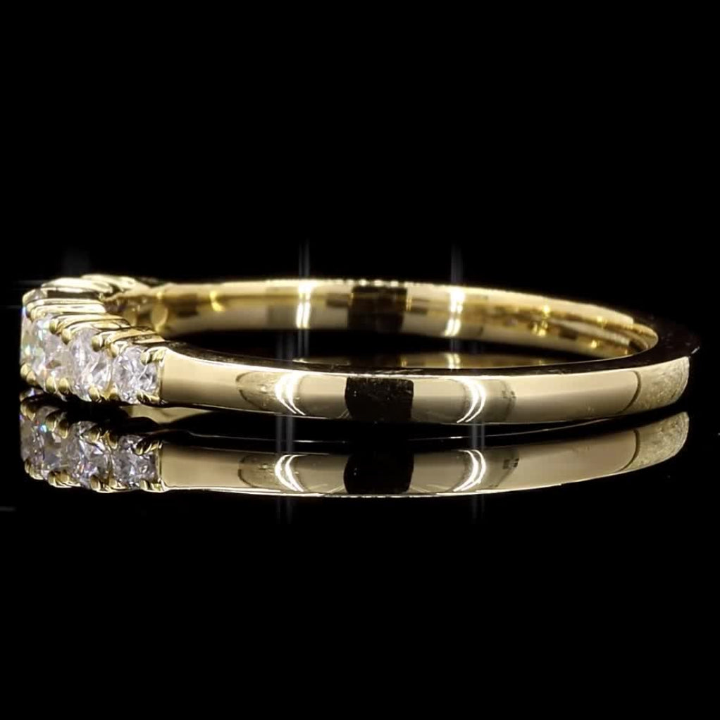 A yellow gold ring with a cluster of small clear gemstones on the band, shown against a solid black background with a soft reflection below.