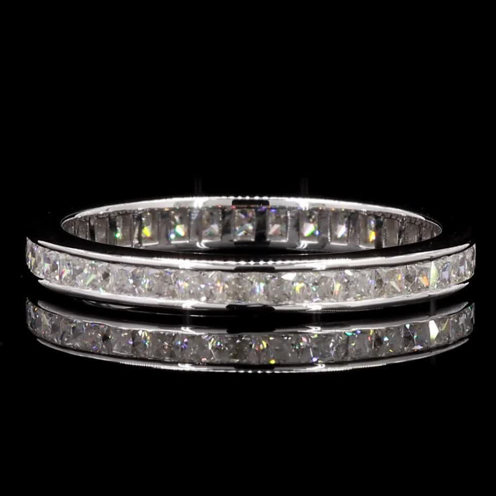 A silver-toned eternity ring with a continuous channel setting of clear stones, shown against a solid black background with a soft reflection below.