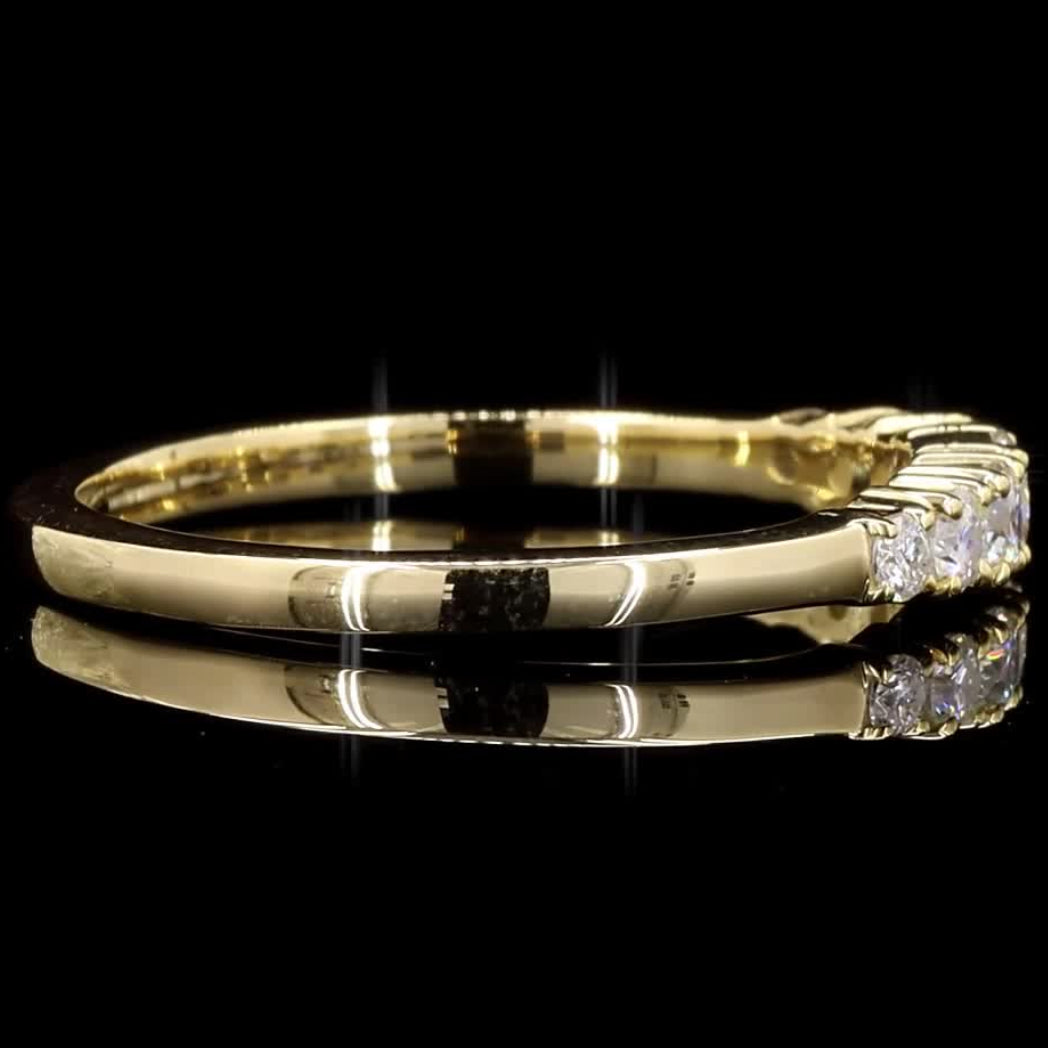 A yellow gold ring with a small cluster of clear gemstones on the right side, photographed on a glossy black reflective surface against a black background.
